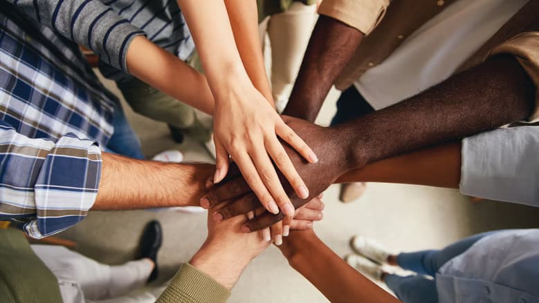 People standing in a circle stacking their hands to show unity.